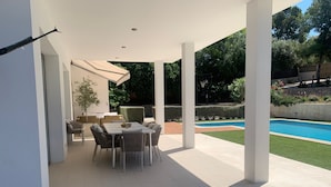 Un portico coperto con tavolo e sedie, una piscina e un giardino curato.
