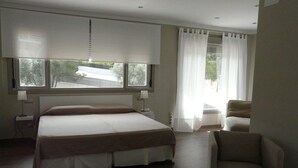 Una camera d'albergo moderna con un letto grande, una poltrona, una scrivania e una finestra con tende.