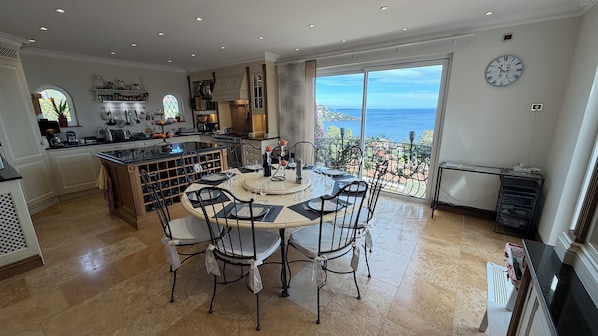Une cuisine spacieuse avec un coin repas, de grandes fenêtres offrant une vue sur la mer et une horloge au mur.