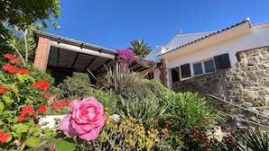 A house with a stone wall, a covered patio, and a garden with various plants and flowers. - 5-star villa. Air-conditioned. Secure. Exceptional sea view, Swimming pool (Saint-Raphaël)
