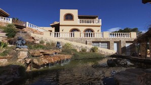 A Mediterranean-style building with a stone facade, a water feature, and a stone pathway leading to the entrance.