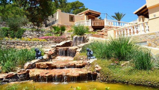 A landscaped garden with a cascading waterfall, stone steps, and statues.