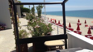 Un balcon donnant sur une plage, avec des parasols rouges et des chaises longues.