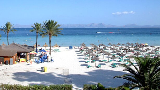 A beach with palm trees, umbrellas, and a building with a thatched roof. - Ground floor with garden and barbecue, 5 minutes from the beach (Alcudia)