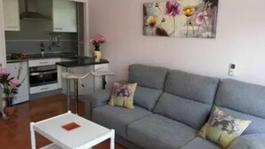 A living room with a grey sofa, a white coffee table, and a kitchen in the background. - Ground floor with garden and barbecue, 5 minutes from the beach (Alcudia)