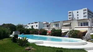A hotel with a swimming pool surrounded by greenery and white buildings. - Ground floor with garden and barbecue, 5 minutes from the beach (Alcudia)