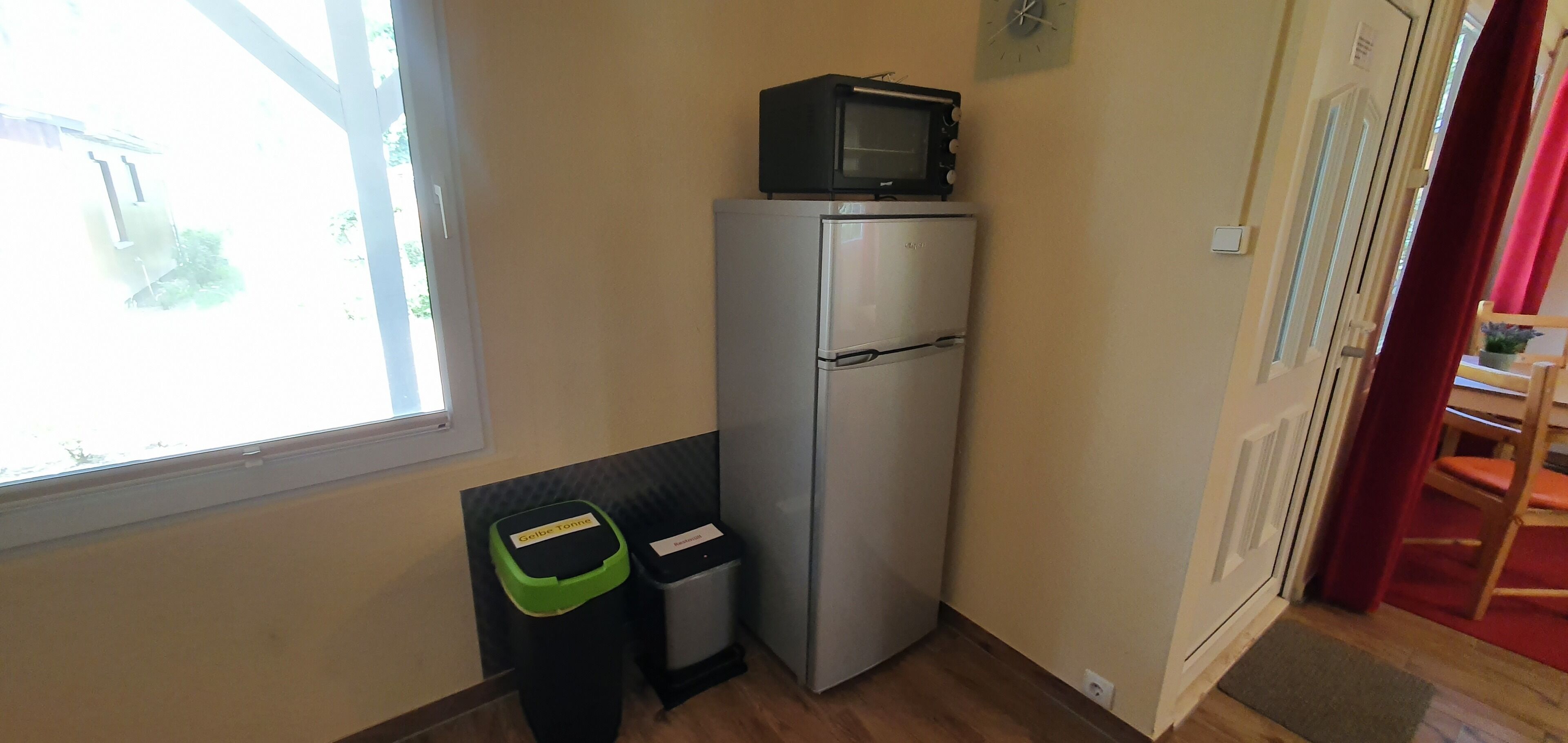 A compact kitchen with a refrigerator, a microwave, and a trash bin.