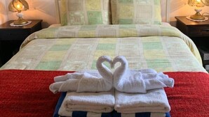 Ein ordentlich bezogenes Bett mit roter Decke, einer Handtuch-Arrangement in Herzform und einem Gemälde von roten Blumen an der Wand.