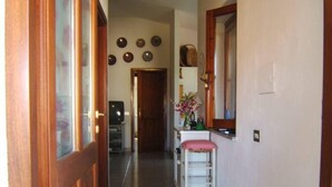 A hallway with a wooden door, a white bench, a mirror, and a wall with decorative plates. - Apartment/ flat - Budoni (Budoni)