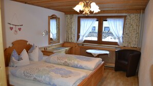 A wooden bed with floral bedding, a wooden desk, a chair, and a window with curtains.