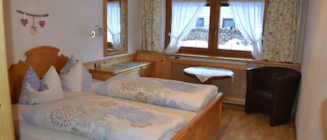 A wooden bed with floral bedding, a wooden desk, a chair, and a window with curtains.