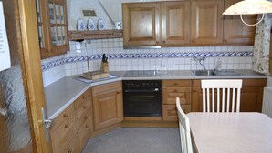 A kitchen with wooden cabinets, a white countertop, a black oven, and a white chair.
