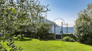 Un jardin situé sur la côte, agrémenté d’un portail en métal, d’un lampadaire et offrant une vue sur la mer.