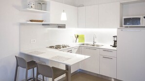 Une cuisine compacte avec des meubles blancs, une cuisinière à gaz, un évier et un four à micro-ondes. Il y a deux chaises autour de la table à manger et un luminaire suspendu.