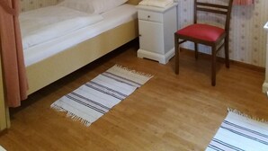 A single bed with a canopy, a bedside table, a chair, a small heater, and a window with curtains. - Forest, water, stone, "small Canada" in the middle of Saxony. (Kirchberg)