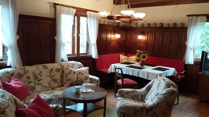 A cozy dining area with a wooden table, red upholstered bench, and floral-patterned sofas. - Forest, water, stone, "small Canada" in the middle of Saxony. (Kirchberg)