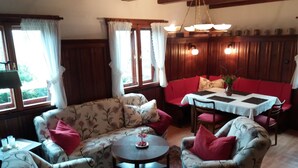 A cozy living room with floral patterned sofas, a round coffee table, and a dining table with red cushions. - Forest, water, stone, "small Canada" in the middle of Saxony. (Kirchberg)