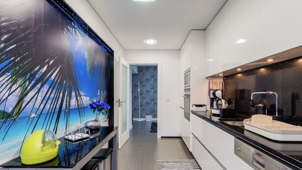 Eine moderne Küche mit weißen Schränken, einer schwarzen Arbeitsplatte und einem großen Fenster mit einem tropischen Wandbild.