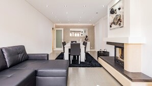Ein modernes Wohnzimmer mit einer schwarzen Ledersofa, einem Esstisch mit Stühlen, einem Kamin und einem an der Wand hängenden Kunstwerk.