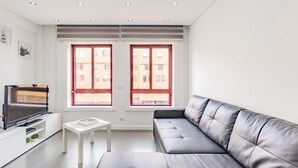 Ein modernes Wohnzimmer mit einem grauen Ledersofa, einem Flachbildfernseher auf einem weißen Schrank und einem kleinen weißen Tisch.