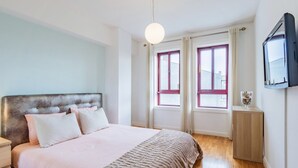 Ein Schlafzimmer mit Bett, Nachttisch, Fernseher und einem Fenster mit Vorhängen.