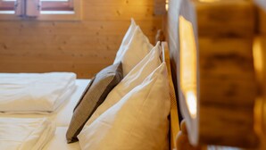 Un lit avec du linge de lit blanc et un coussin à carreaux, une tête de lit en bois et une fenêtre donnant sur l’extérieur.