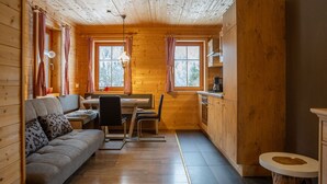 Un intérieur de chalet chaleureux avec un canapé, une table à manger, des chaises et un coin cuisine.