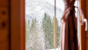 Une vue sur une forêt enneigée, avec une montagne en arrière-plan, telle qu'elle apparaît à travers une fenêtre.