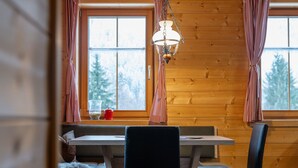 L’intérieur d’une cabane en bois, avec une table à manger, des chaises, un banc et un luminaire suspendu.