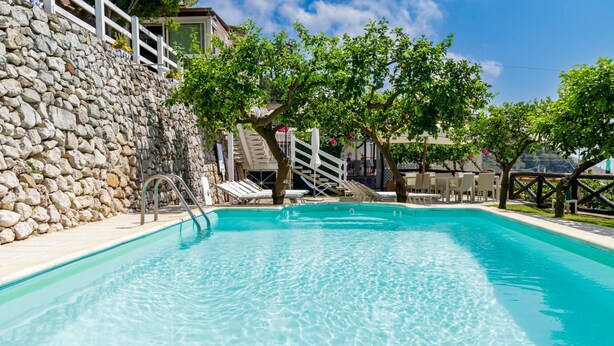 Une piscine à l’eau d’un bleu cristallin, entourée d’un mur de pierre et d’une terrasse en bois.