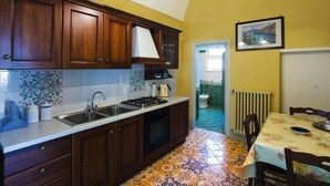 Une cuisine avec des armoires en bois, un évier et une cuisinière. On y trouve une table à manger avec des chaises et un tableau accroché au mur.