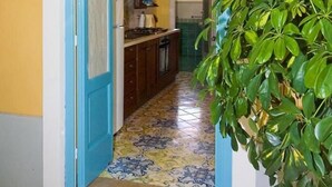 Un couloir étroit avec une porte bleue qui donne sur une cuisine équipée de meubles en bois et dont le sol est carrelé.