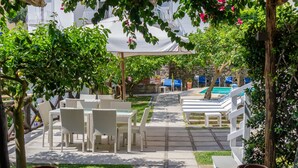 Un espace extérieur aménagé en terrasse, avec des meubles en osier blanc, une piscine et un mur de pierre en arrière-plan.