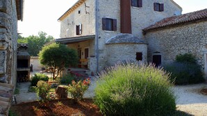 Un edificio in pietra con aspetto rustico, un camino e un giardino con diverse piante e una panchina in legno.