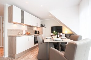 A modern kitchen with white cabinets, a dining area with a table and chairs, and a TV mounted on the wall.
