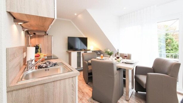 Une cuisine moderne équipée d’une cuisinière intégrée, d’un évier et d’un téléviseur à écran plat. On y trouve également un coin repas avec une table et des chaises, ainsi qu’une grande fenêtre offrant une vue sur la verdure environnante.