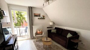 Un salon moderne avec un canapé, un fauteuil, une table basse et un téléviseur posé sur un meuble.