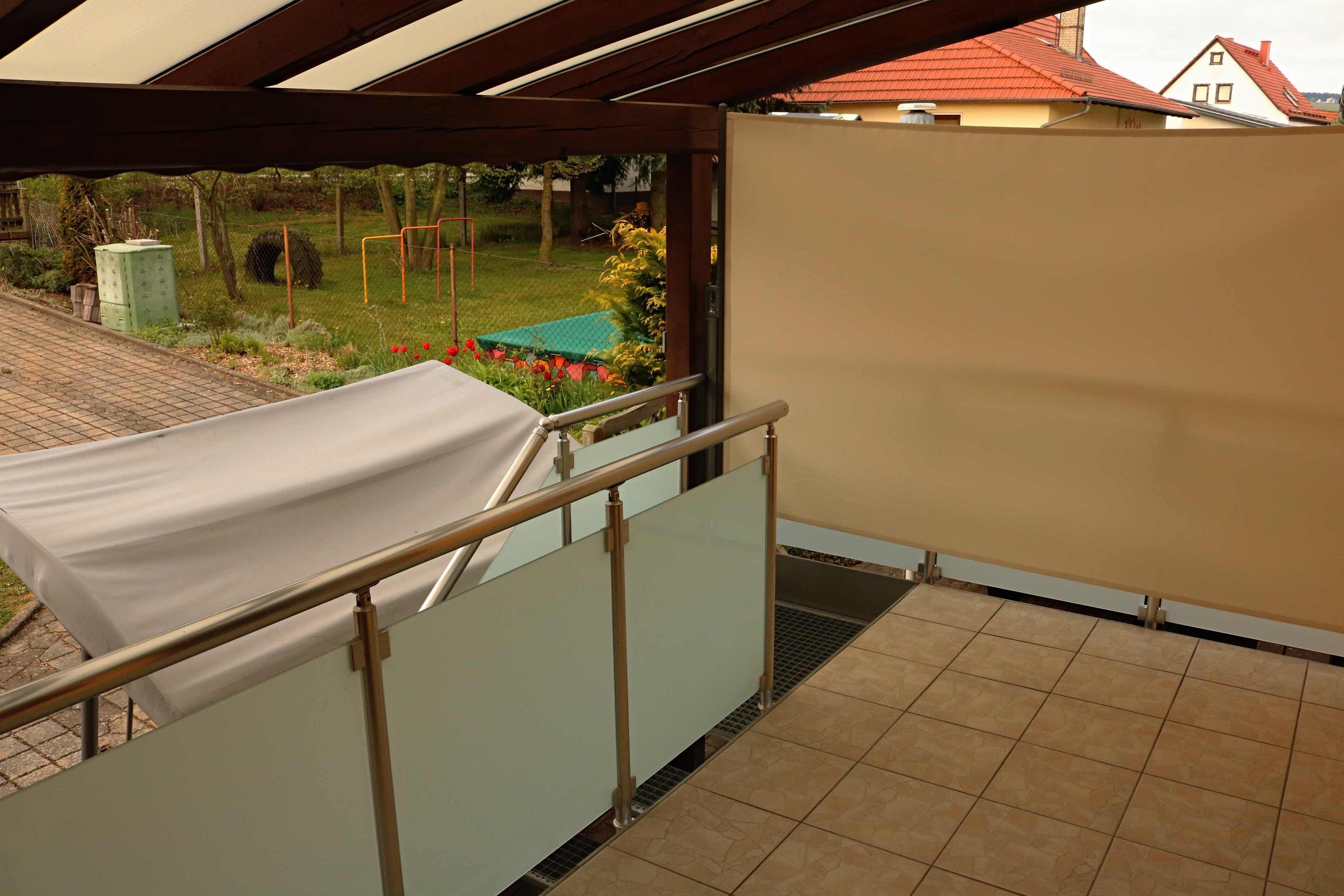 A balcony with a white table, metal railing, and a view of a garden and houses in the background.