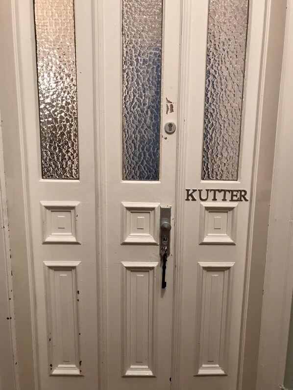 A white door with three panels, each featuring a textured glass window. The middle panel has a keyhole and a key inserted. The right panel has the word "KUTTER" written on it.