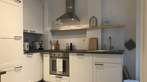 A modern kitchen with white cabinets, a stainless steel range hood, and a wooden countertop.