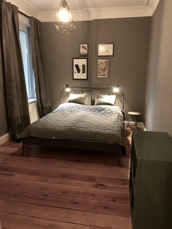 A bedroom with a bed, a bedside table, a lamp, and a wall-mounted light fixture.