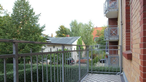 A balcony with a checkered floor, metal railing, and a view of a residential area with trees and parked cars. - Apartment in Potsdam - Berlin suburb - near Holy Lake -<br><br> (Potsdam)