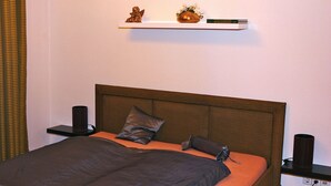 A bedroom with a bed, pillows, a nightstand, a shelf with decorative items, and a wall socket. - Apartment in Potsdam - Berlin suburb - near Holy Lake -<br><br> (Potsdam)