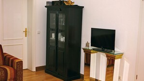 A living room with a black cabinet, a television on a glass-top stand, and a patterned sofa. - Apartment in Potsdam - Berlin suburb - near Holy Lake -<br><br> (Potsdam)