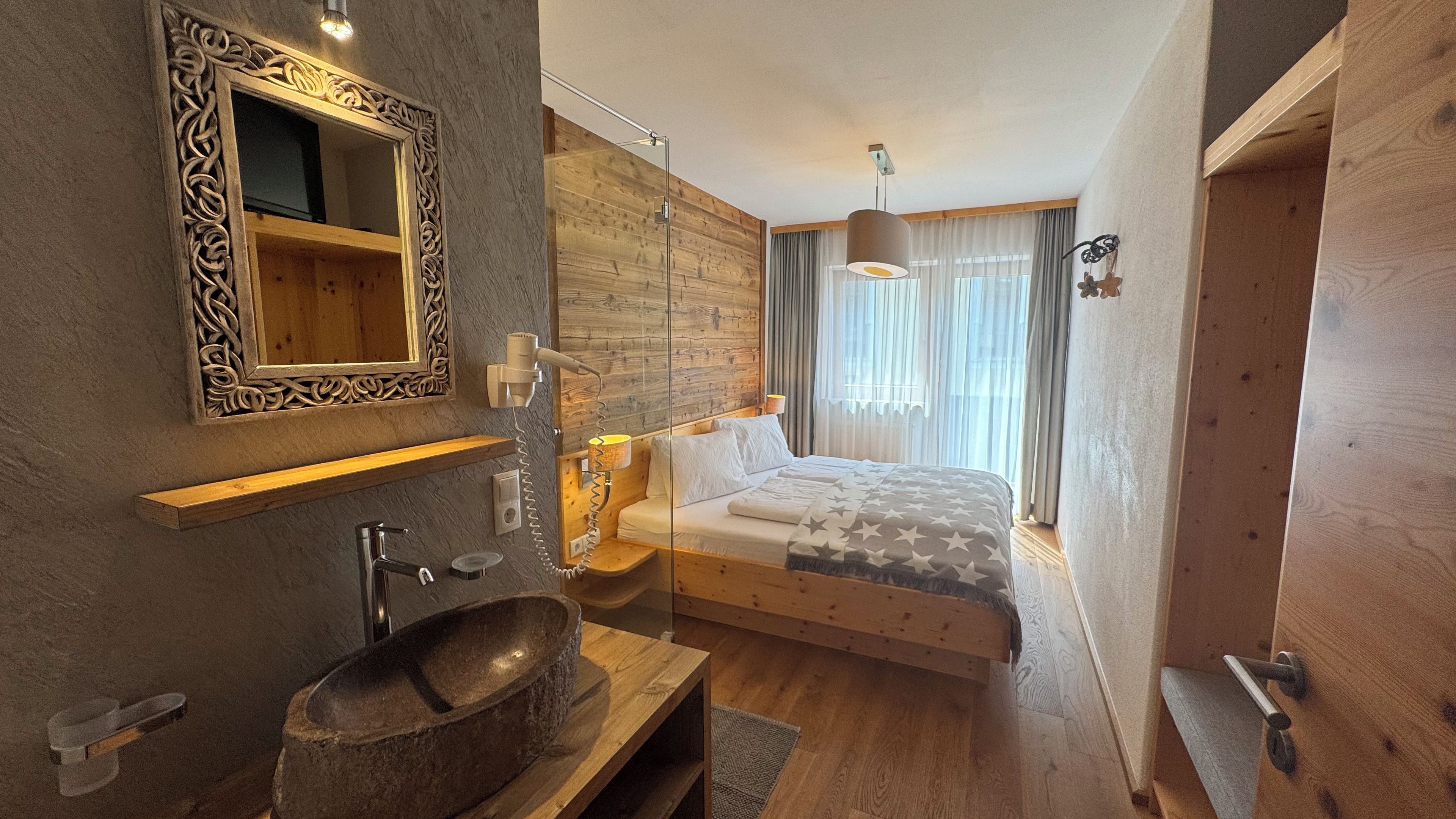 A modern bedroom with a wooden headboard, a large bed, a bedside table with a lamp, and a mirror with an ornate frame.