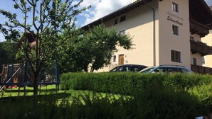 A building with a clock tower, labeled "Appartements Schweiberer," surrounded by greenery and parked cars. - Schweiberer Apartments - Fine Living & Garden (Ried im Zillertal)