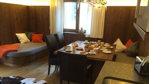 A cozy dining area with a wooden table set for breakfast, a sofa with cushions, and a large window with curtains. - Appartements Schweiberer, exclusive apartment Hambergblick (Ried im Zillertal)