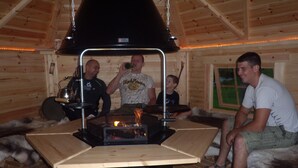 A cozy cabin interior with a central wood-burning stove, wooden walls, and a window with a view. - Appartements Schweiberer, exclusive apartment Hambergblick (Ried im Zillertal)