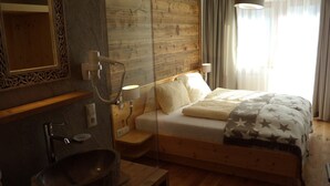A wooden bedroom with a bed, bedside lamps, a mirror, and a wooden nightstand. - Appartements Schweiberer, exclusive apartment Hambergblick (Ried im Zillertal)