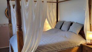 Uma cama de dossel com estrutura de madeira, cabeceira de madeira e mesa de cabeceira com abajur.